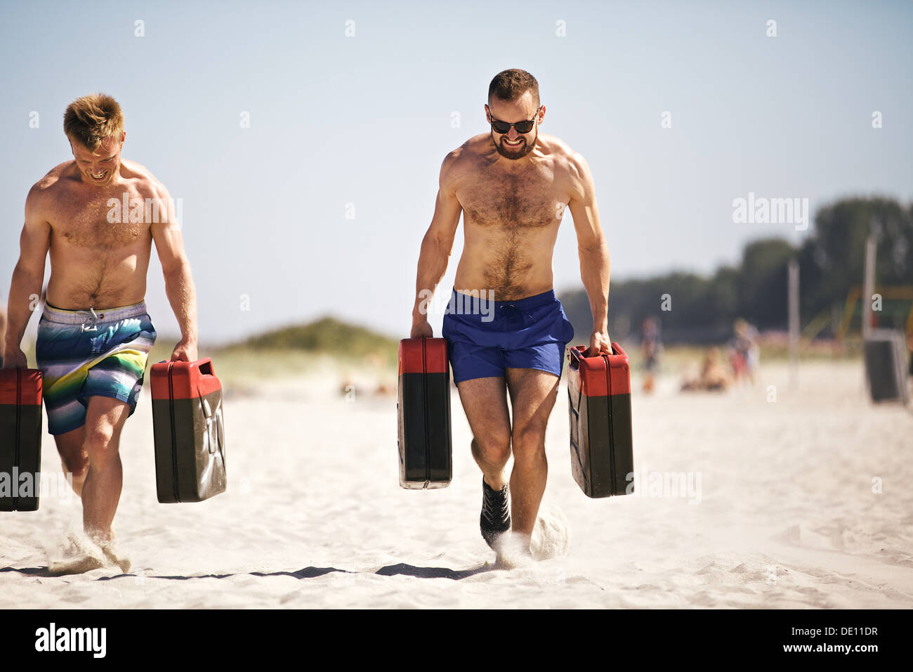 Forte ragazzi crossfit sollevamento bidoni pesanti al di fuori sulla spiaggia. Muscolare di persone attive in 20s la formazione per mantenere sana la vita Foto Stock