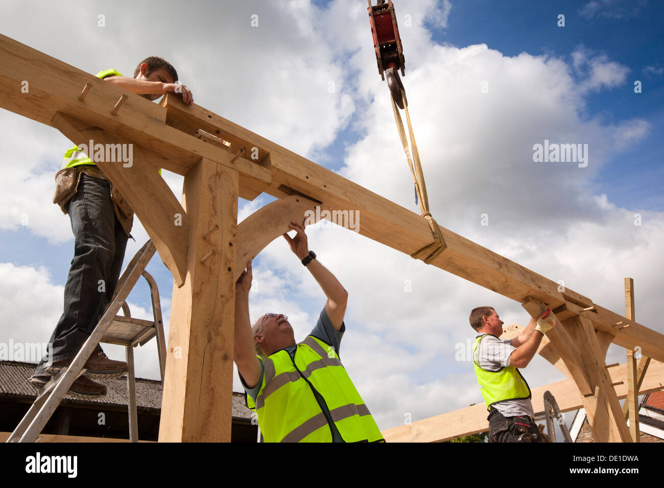 Auto costruzione di casa, costruendo verde legname di quercia incorniciato struttura, utilizzando ingaggiato gru per il sollevamento pesante telaio in legno Foto Stock