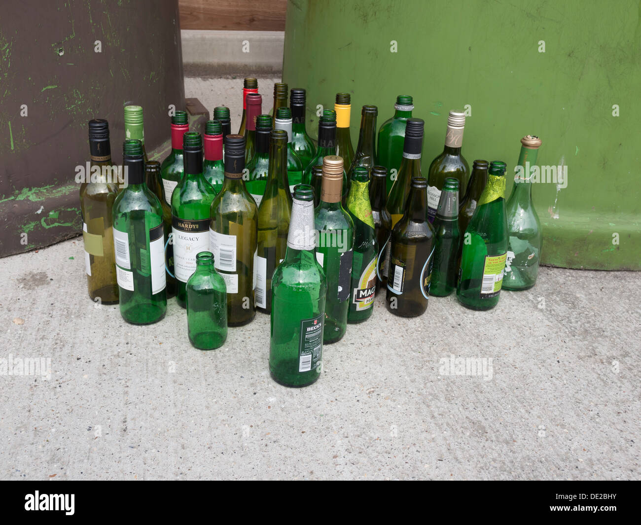 Bottiglie impilate ordinatamente accanto a un intero contenitore di riciclaggio per il vetro misto Foto Stock