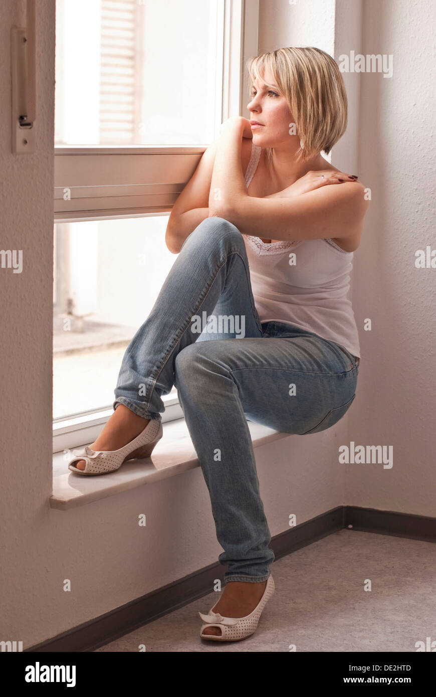 Giovane donna seduta da una finestra Foto Stock