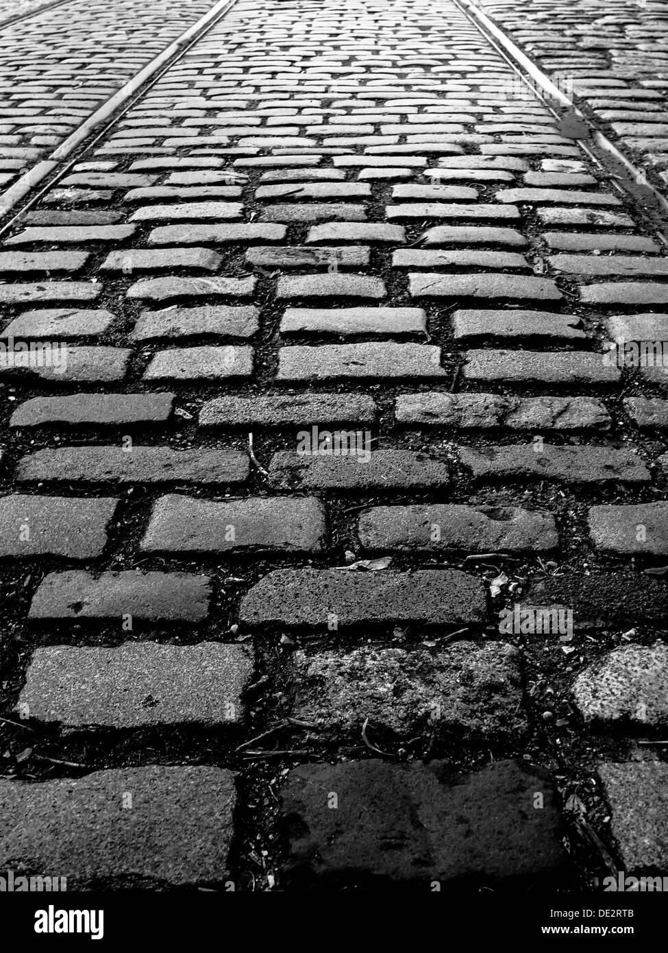 Fotografia in bianco e nero di una strada di ciottoli con i binari del tram. Foto Stock