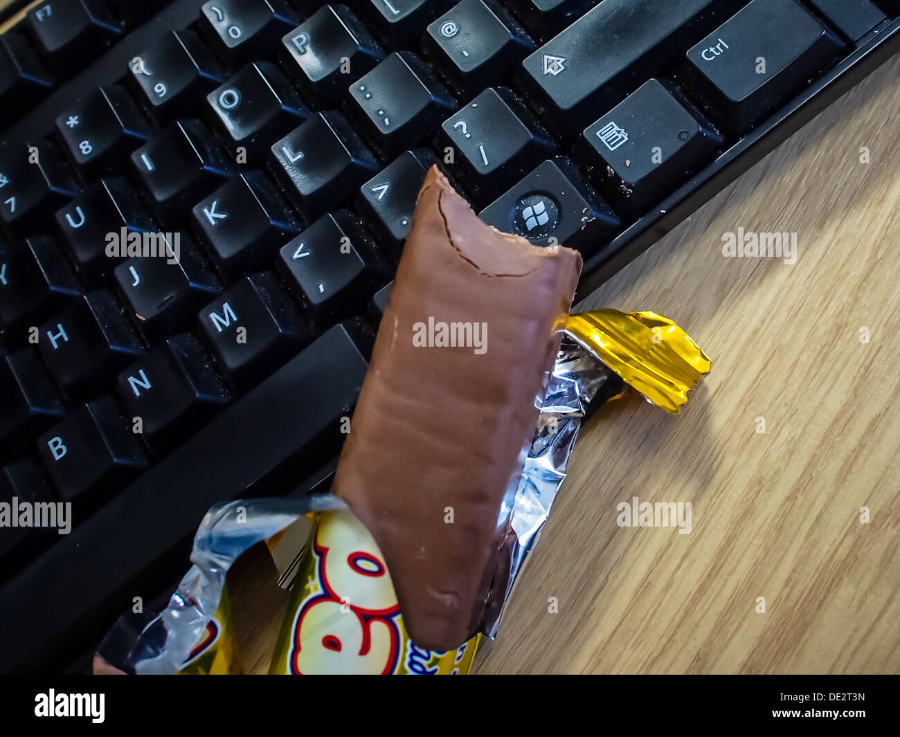Una barra di cioccolato su una tastiera di sporco causato da snacking in corrispondenza di una stazione di lavoro Foto Stock