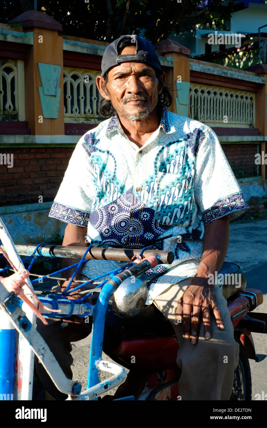 Local uomo seduto sul suo becak motorizzato al di fuori di una casa in java indonesia Foto Stock