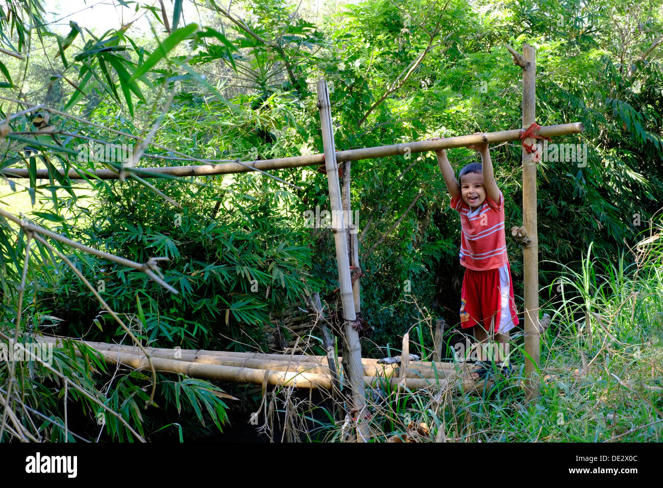 Little Boy giocando su un bambù traballanti ponte sul fiume piccolo nel villaggio rurale di Java in Indonesia Foto Stock