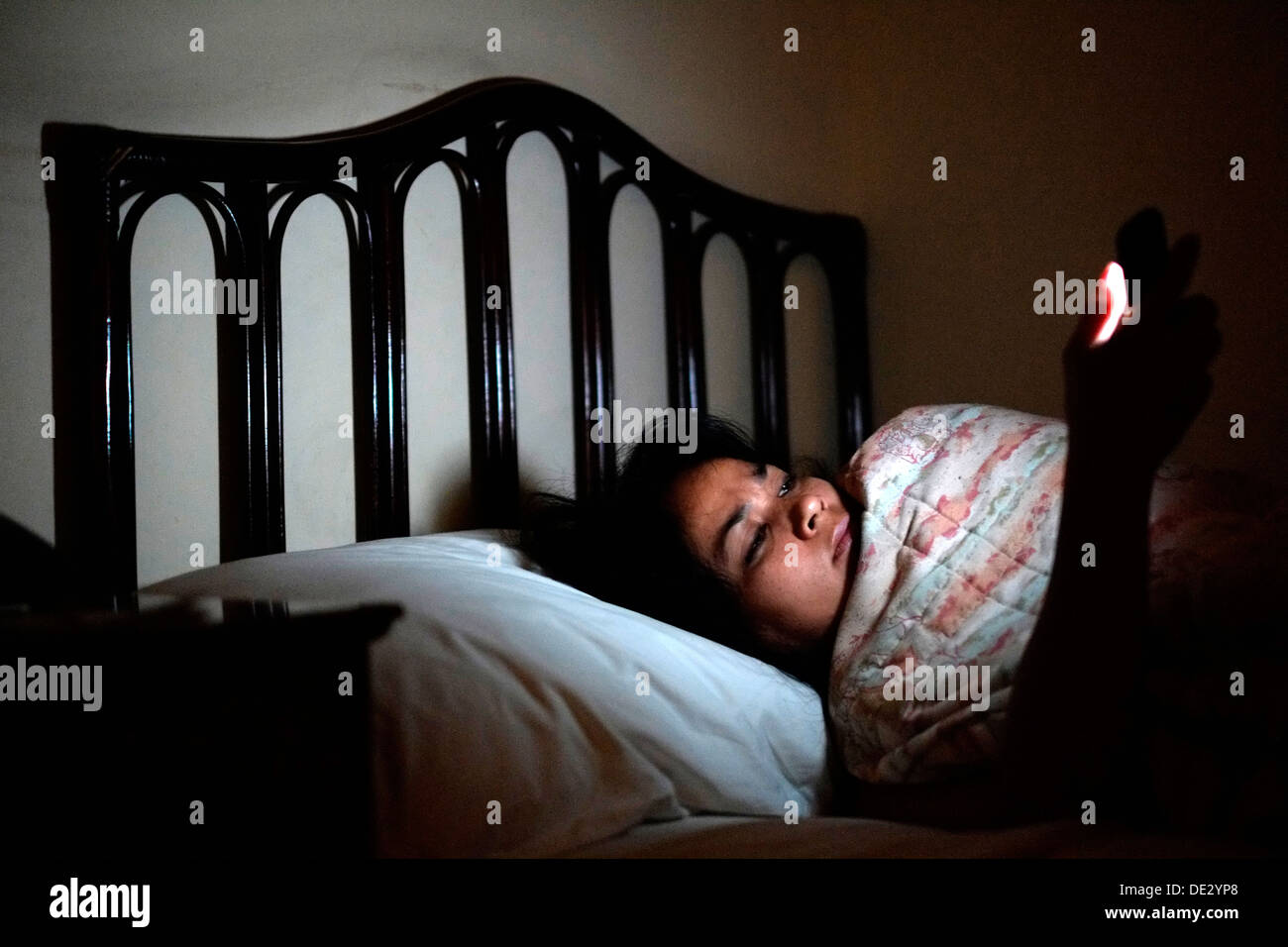 La donna a letto a notte il controllo sociale dei media sul suo telefono mobile Foto Stock