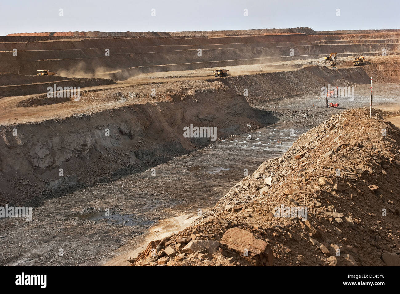 Superficie fossa miniere d'oro, la trapanatura di fori per gli addebiti prima di blast con gli escavatori e haul camion sul banco dietro, Mauritania Foto Stock