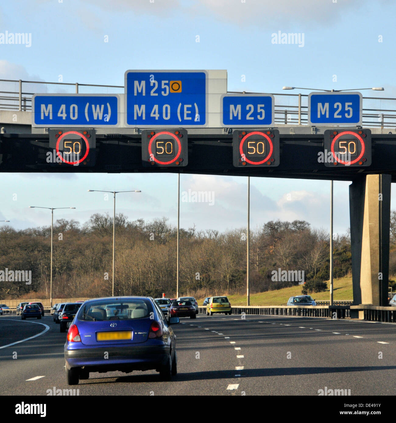 Gli automobilisti che passano sotto i segnali di limite di velocità variabile sul gantry sospeso illuminato sulla strada autostradale M25 UK vicino allo svincolo con M40 London England UK Foto Stock