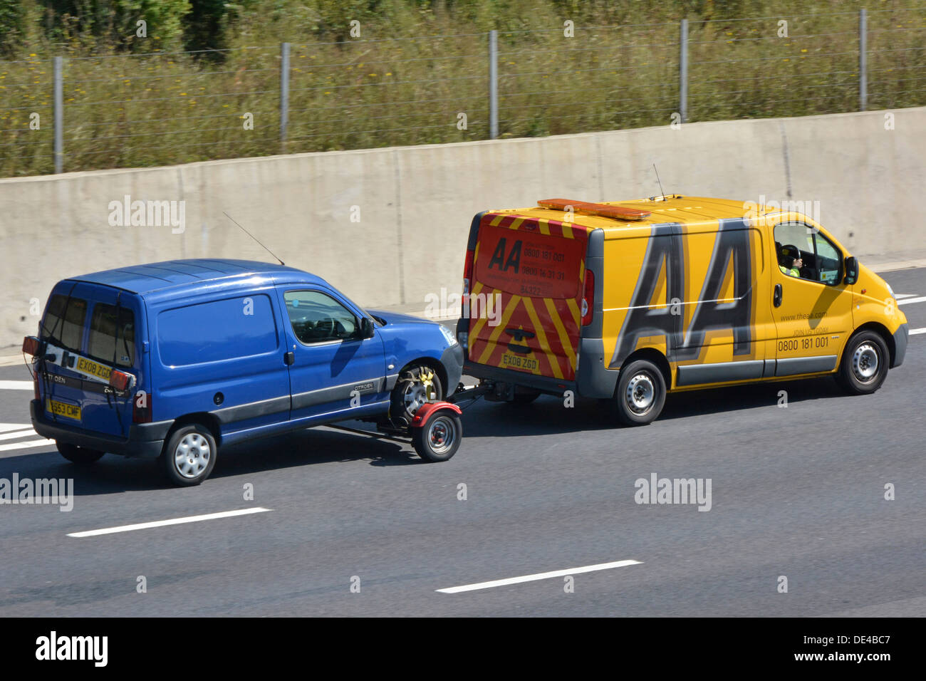 Vista laterale e posteriore del logo su un guasto AA giallo business van e conducente che trainano un furgone blu guasto Percorrere l'autostrada M25 Essex Inghilterra UK Foto Stock