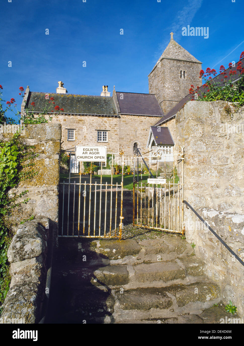 L'approccio a San Seiriol la chiesa, Penmon, Anglesey, e il chiostro corte (ora un giardino) dell'ex convento agostiniano. Cartello bilingue. Foto Stock