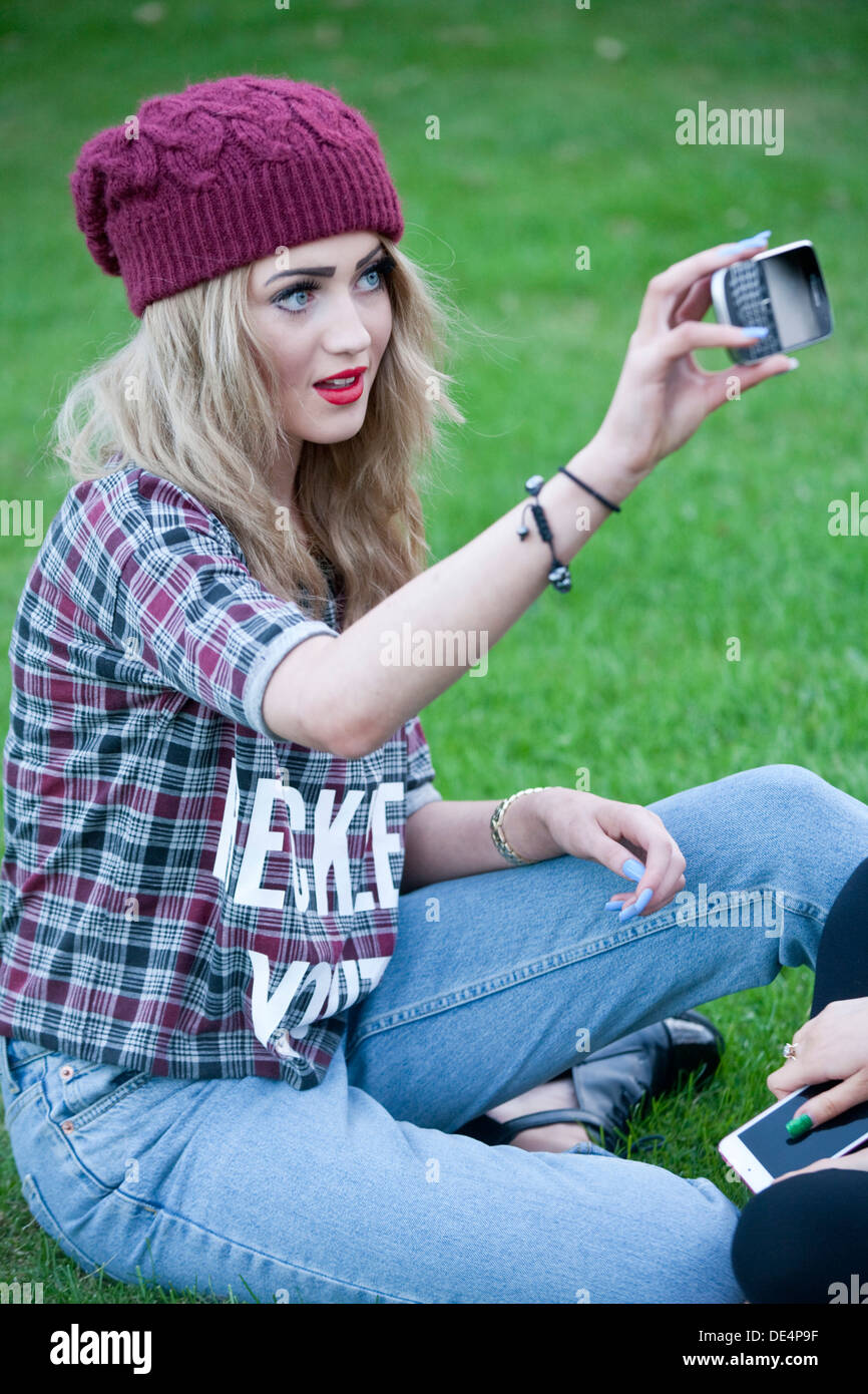 La bionda ragazza adolescente seduto fuori prendendo un autoritratto sul suo telefono. Foto Stock