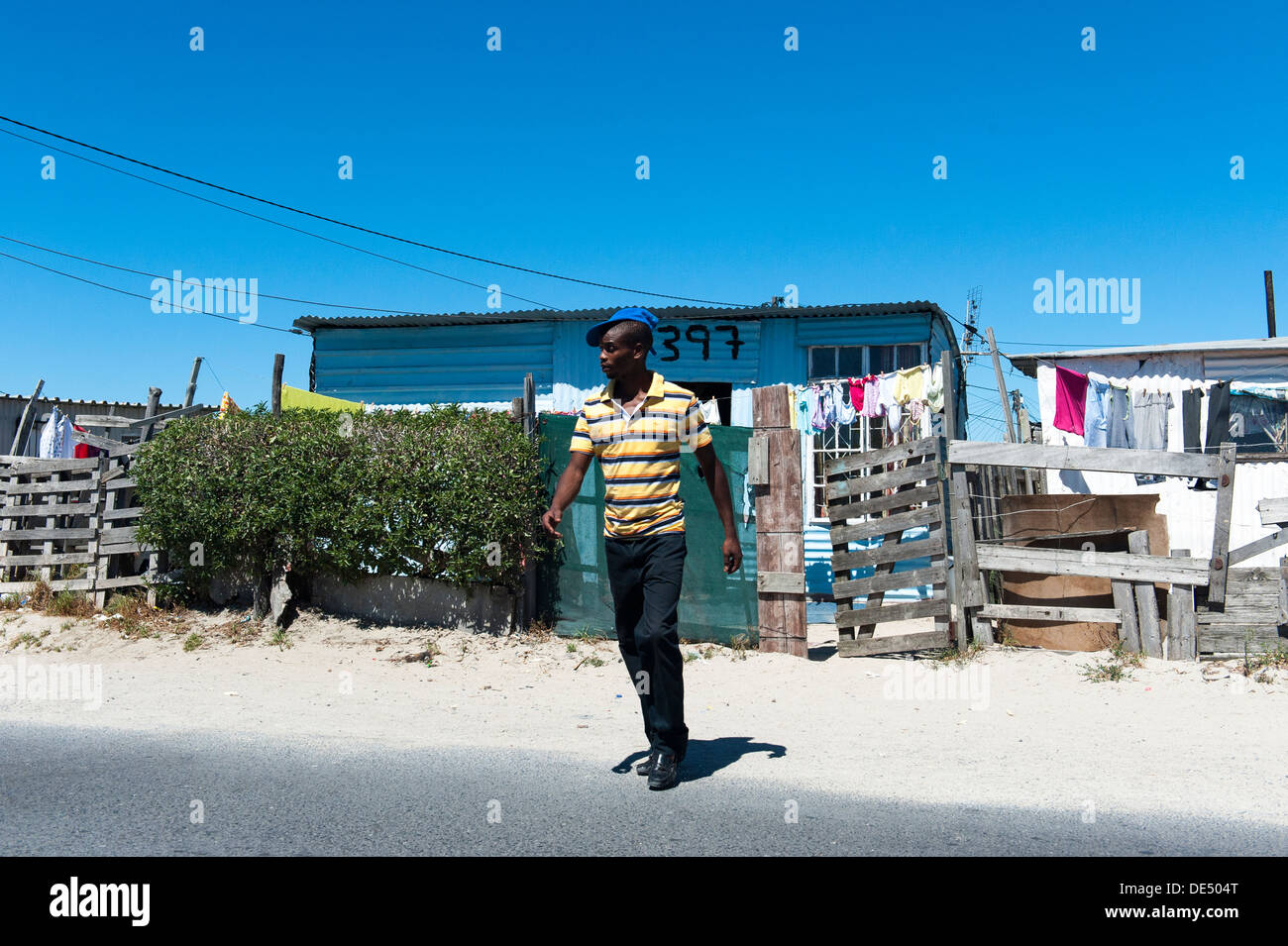 Uomo che attraversa la strada in Khayelitsha, stagno shack in background, Cape Town, Sud Africa Foto Stock