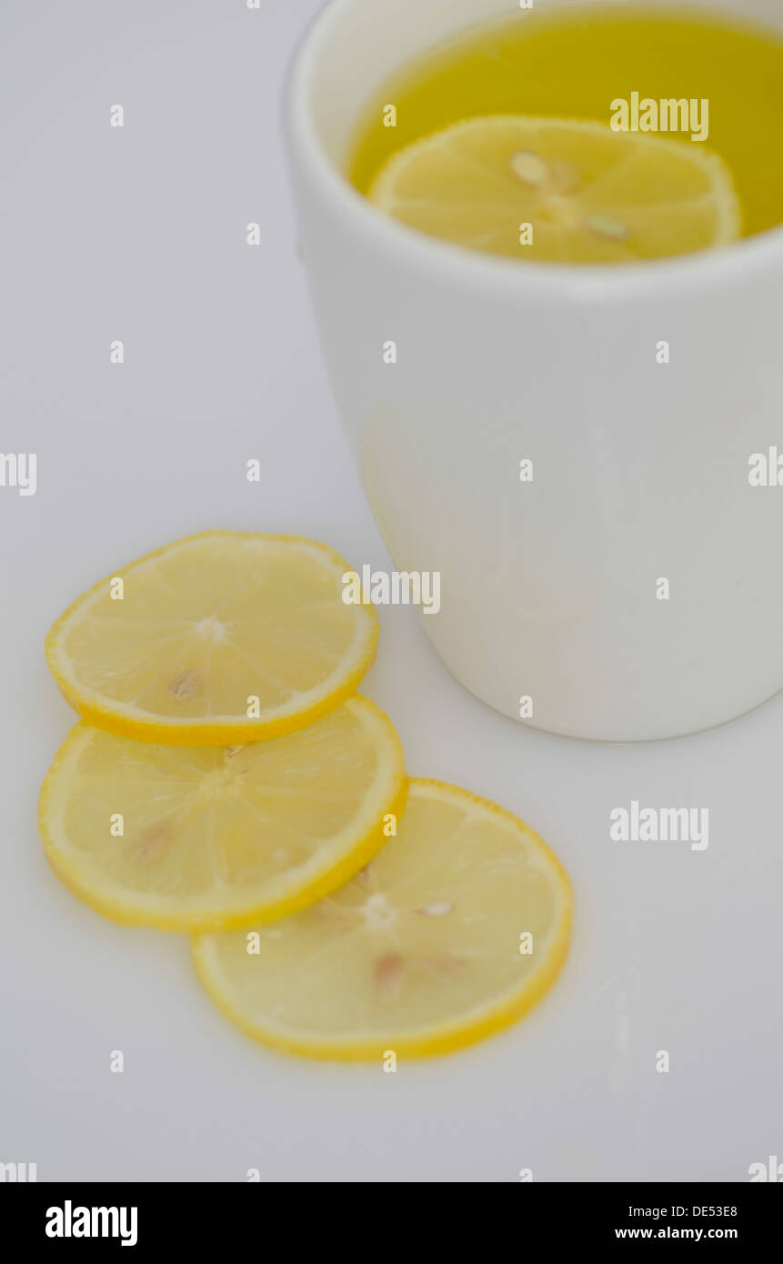 La tazza di acqua calda tè al limone con tre fette sottili di limone visualizzato su una superficie bianca Foto Stock