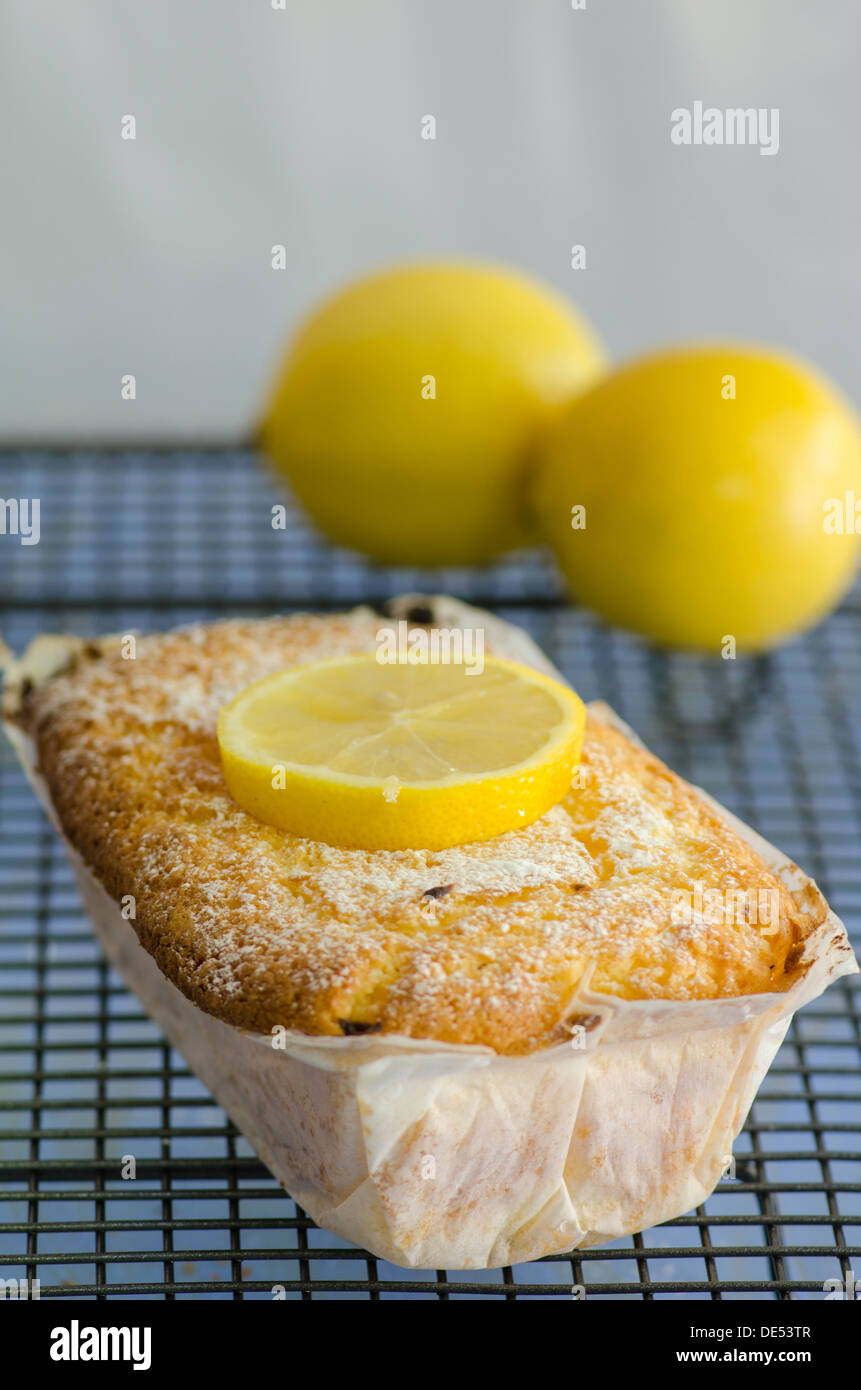 Una deliziosa casa cotto torta al limone avvolto in carta forno e guarnita con spicchi di limone raffreddare su una griglia a filo in cucina Foto Stock