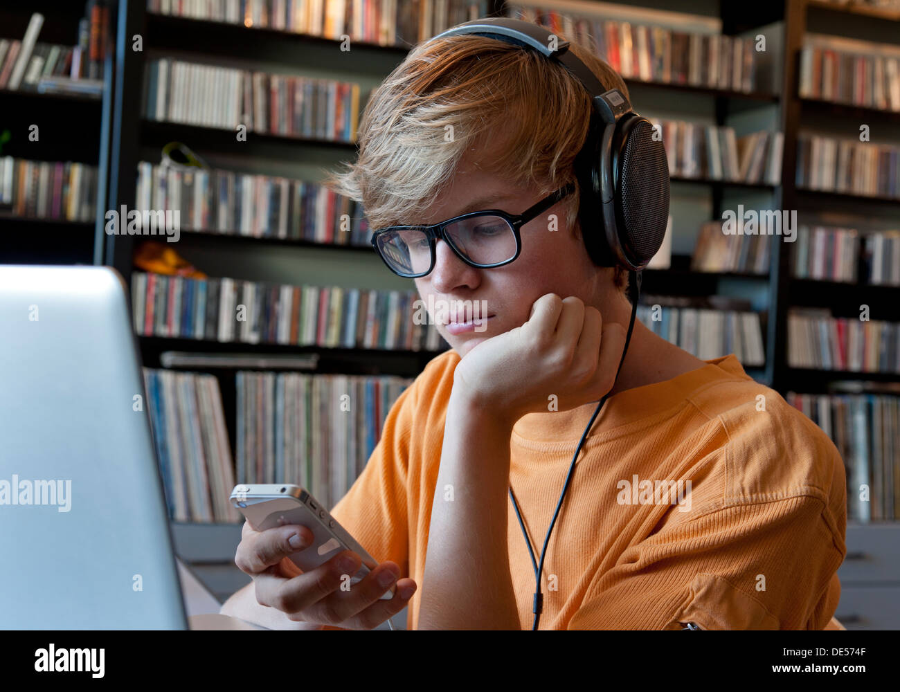 Pensieroso ragazzo adolescente che indossano le cuffie utilizzando il suo smartphone e computer laptop in casa sua libreria musicale Foto Stock
