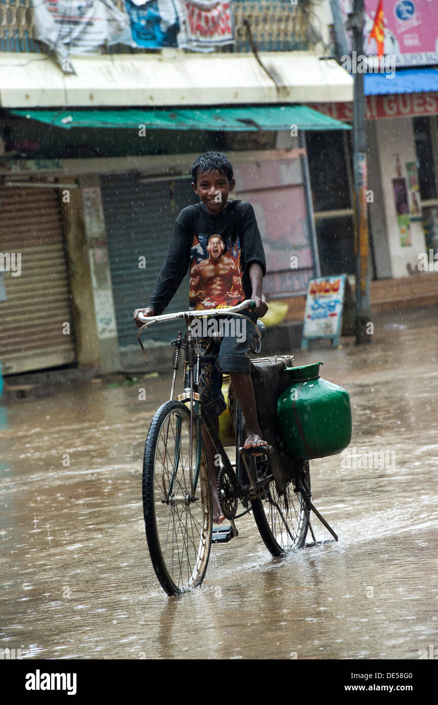 Bassa casta villaggio indiano il ragazzo in bicicletta attraverso una strada allagata durante il monsone. Puttaparthi, Andhra Pradesh, India Foto Stock