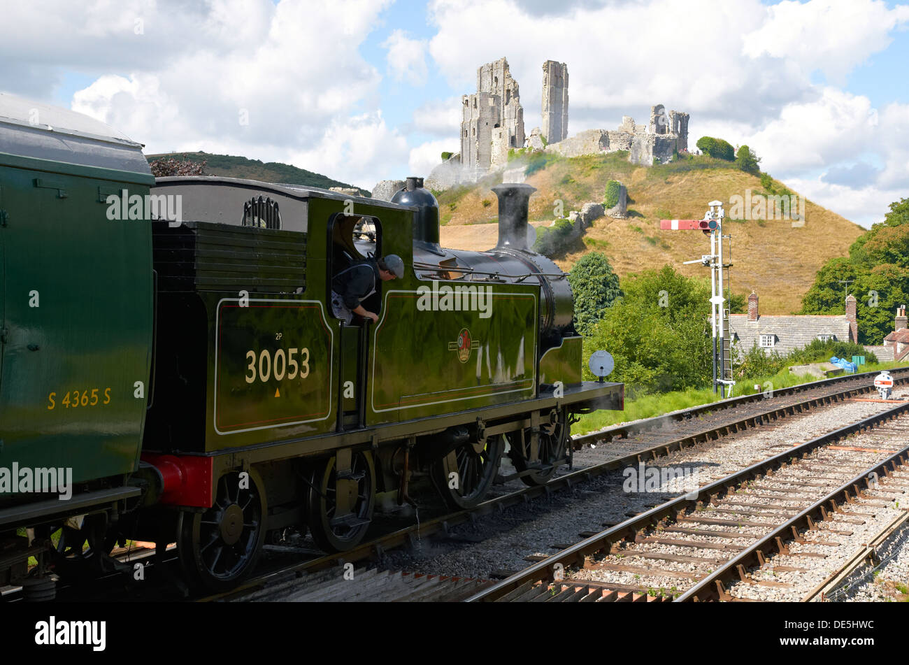 Treno a vapore sulla ferrovia a Swanage in attesa presso Corfe Castle stazione, Dorset, Inghilterra con un treno per Norden. Castello in background. Foto Stock Treno a vapore sulla ferrovia a Swanage in attesa presso Corfe Castle stazione, Dorset, Inghilterra con un treno per Norden. Castello in background. Foto Stock