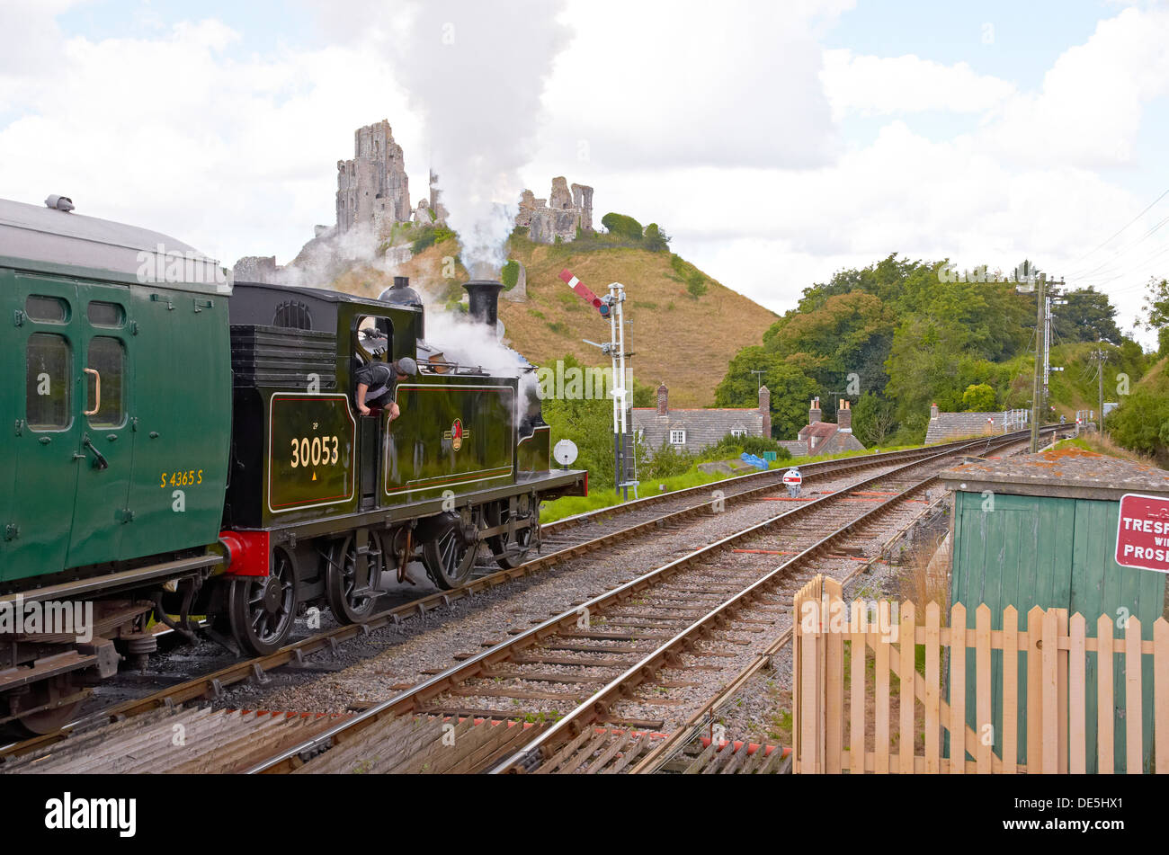 Treno a vapore sulla ferrovia a Swanage in attesa presso Corfe Castle stazione, Dorset, Inghilterra con un treno per Norden. Castello in background. Foto Stock Treno a vapore sulla ferrovia a Swanage in attesa presso Corfe Castle stazione, Dorset, Inghilterra con un treno per Norden. Castello in background. Foto Stock