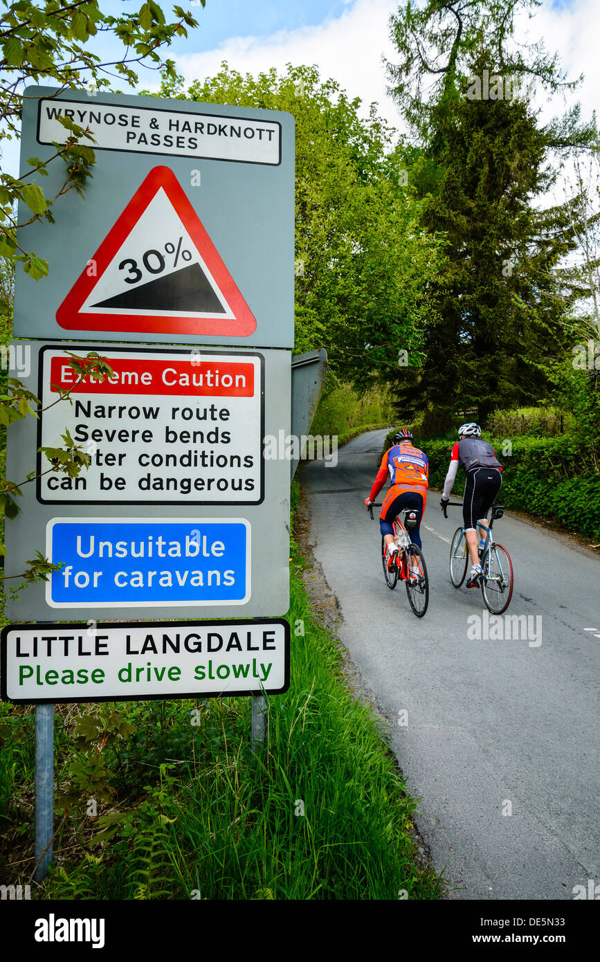 I ciclisti passano i segnali di avvertimento in poco Langdale nel Lake District inglese Foto Stock