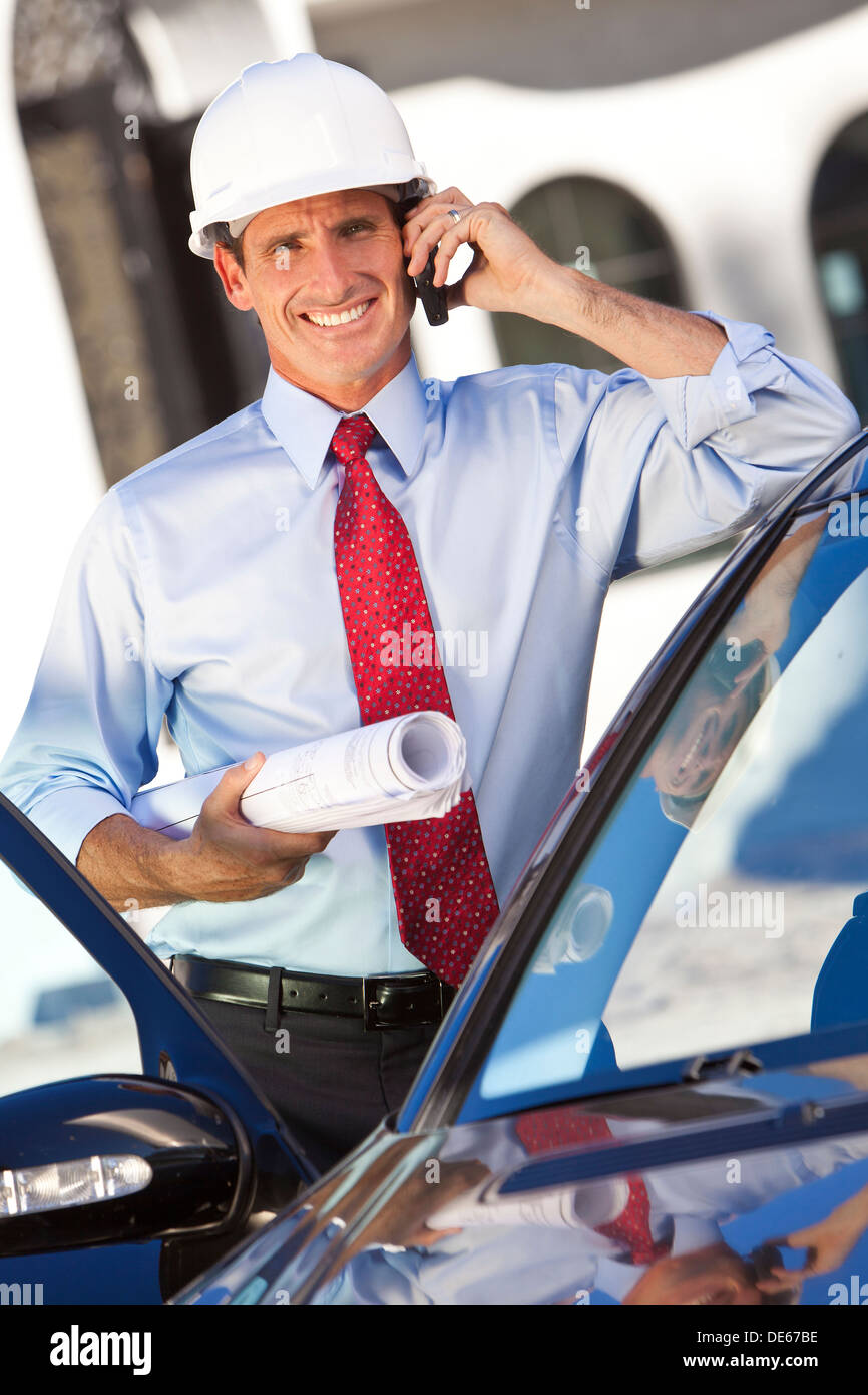 Un imprenditore di successo o di un architetto che indossa un disco bianco hat holding piani & parlando sul suo telefono cellulare in auto Foto Stock