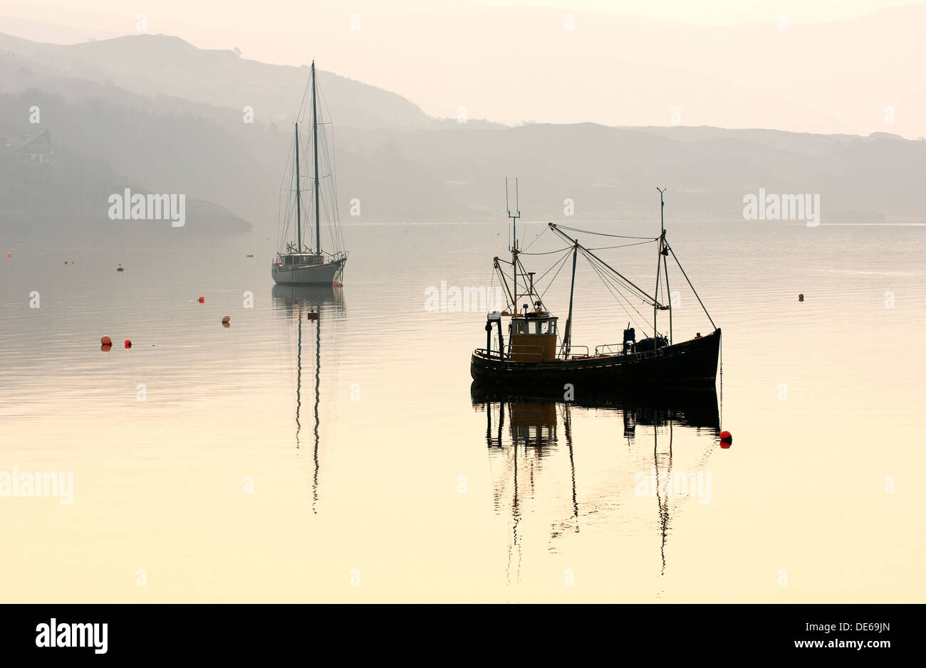 Yacht e la fascia costiera di barca da pesca al di ancoraggio sul Loch Ginestra a Ullapool, regione delle Highlands, a nord-ovest della Scozia, Regno Unito. Alba haze Foto Stock