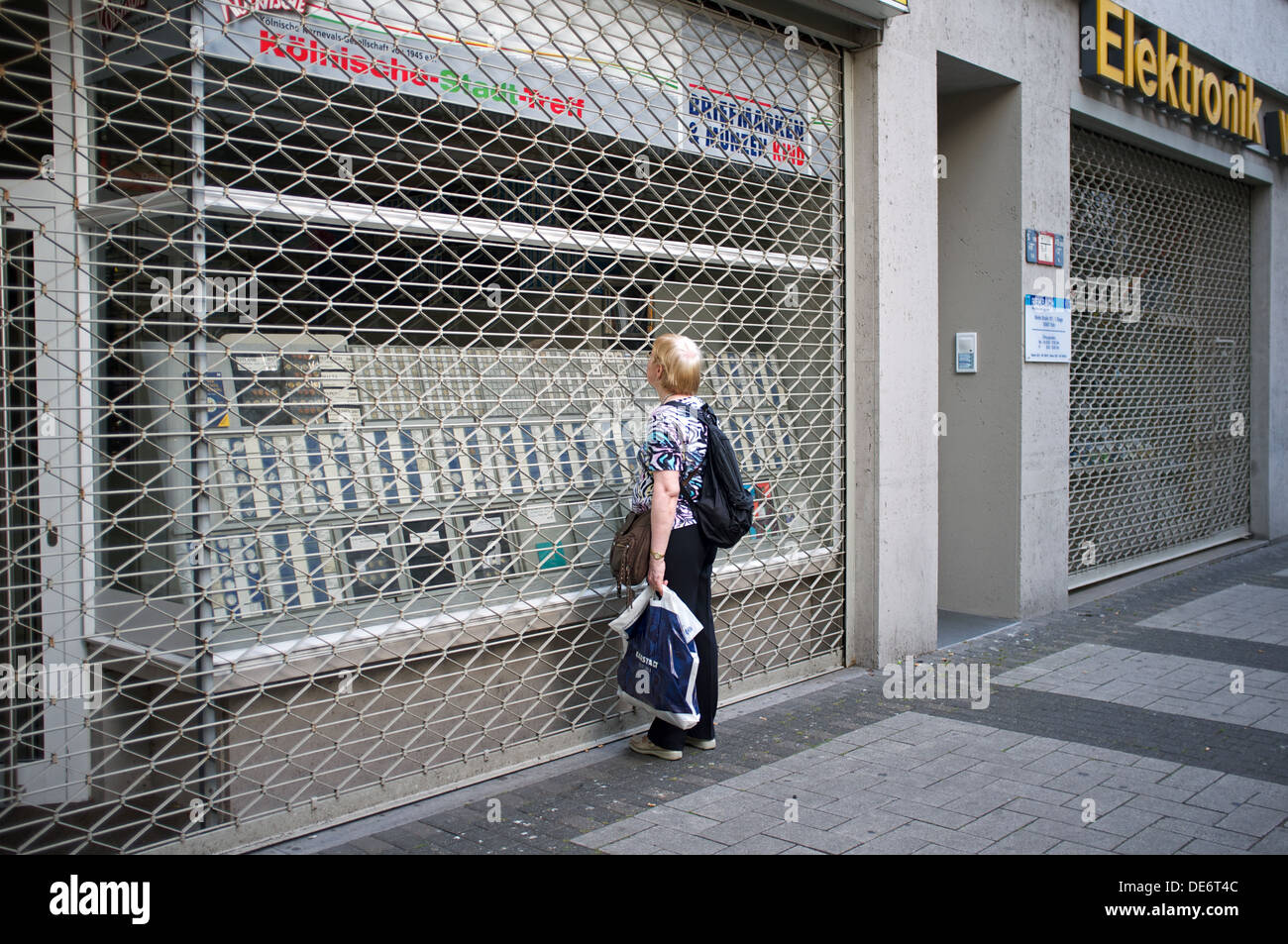 Donna che guarda attraverso le serrande di un negozio chiuso Foto Stock