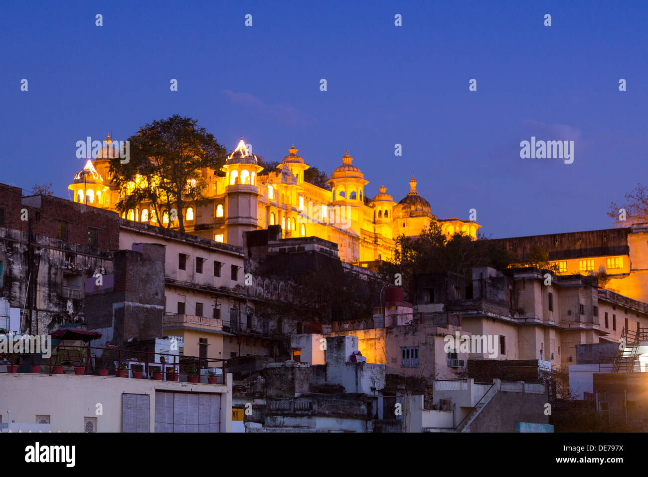India Rajasthan, Udaipur, vista sopra i tetti verso il palazzo di città illuminata al crepuscolo Foto Stock