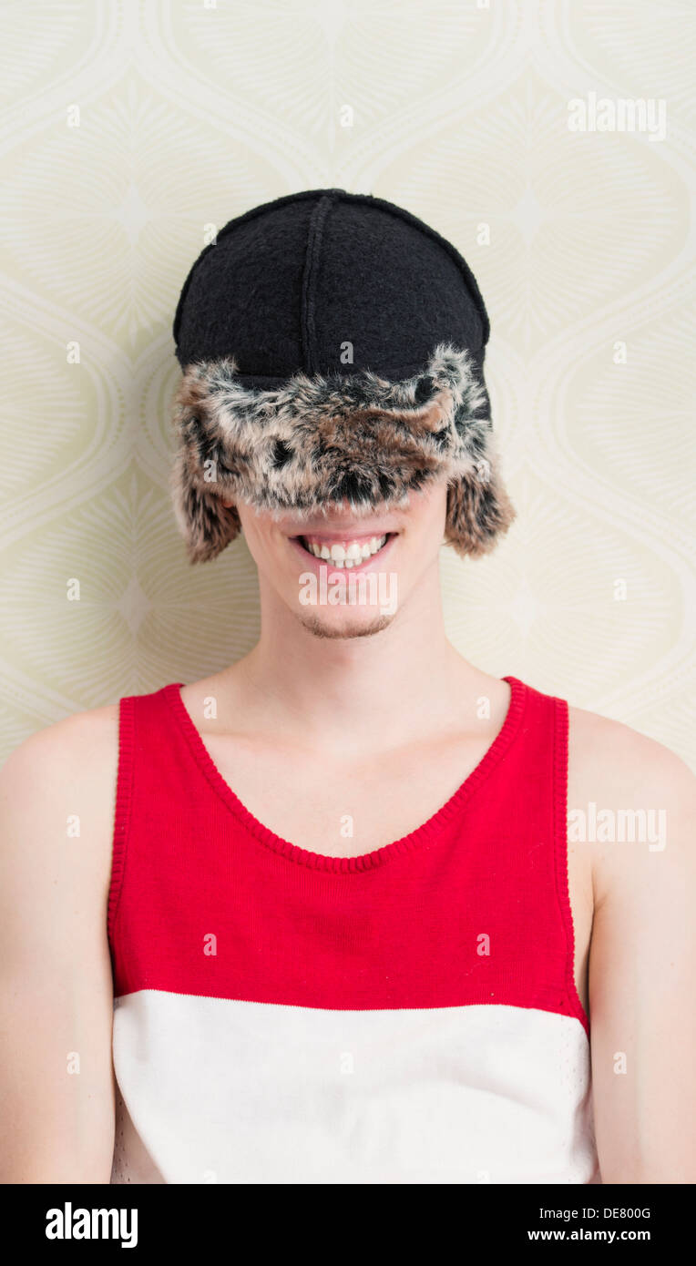 Stile di vita ritratto di ridere giovane con cappello invernale viene tirato verso il basso per coprire i suoi occhi Foto Stock