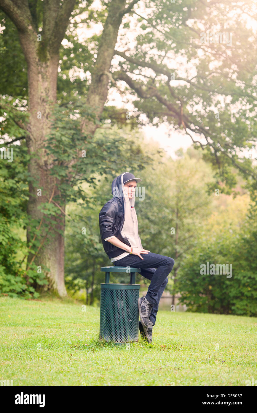 Giovane uomo seduto e in attesa su cestino in un parco Foto Stock