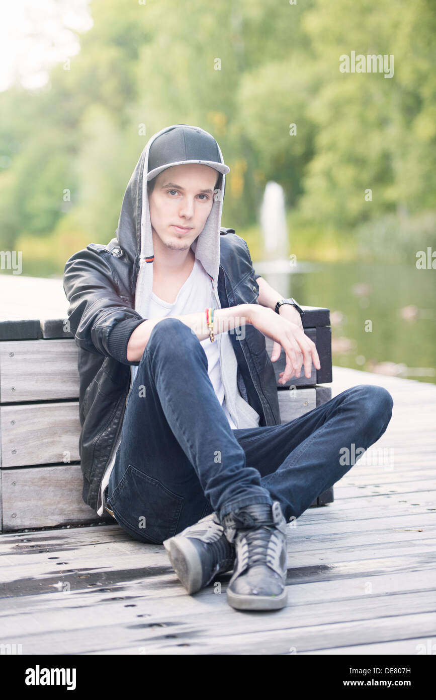 Stile di vita Ritratto di giovane uomo in giacca di pelle seduto in un parco guardando la fotocamera Foto Stock
