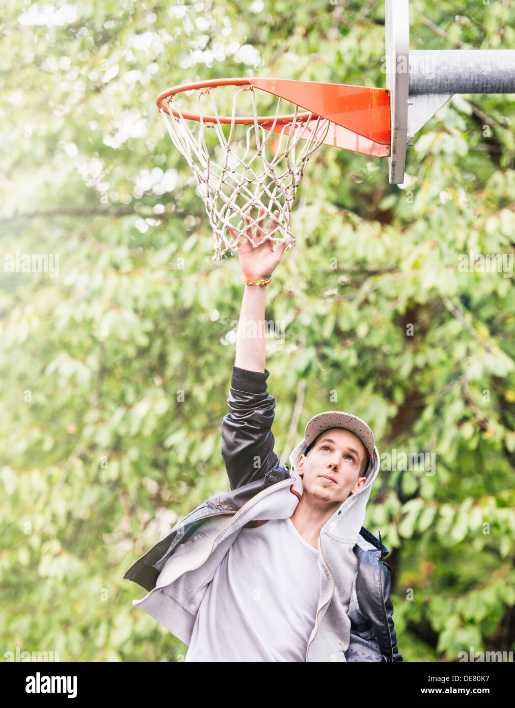 Stile di vita Ritratto di giovane uomo in giacca di pelle di salto e reching per un Basketball hoop Foto Stock