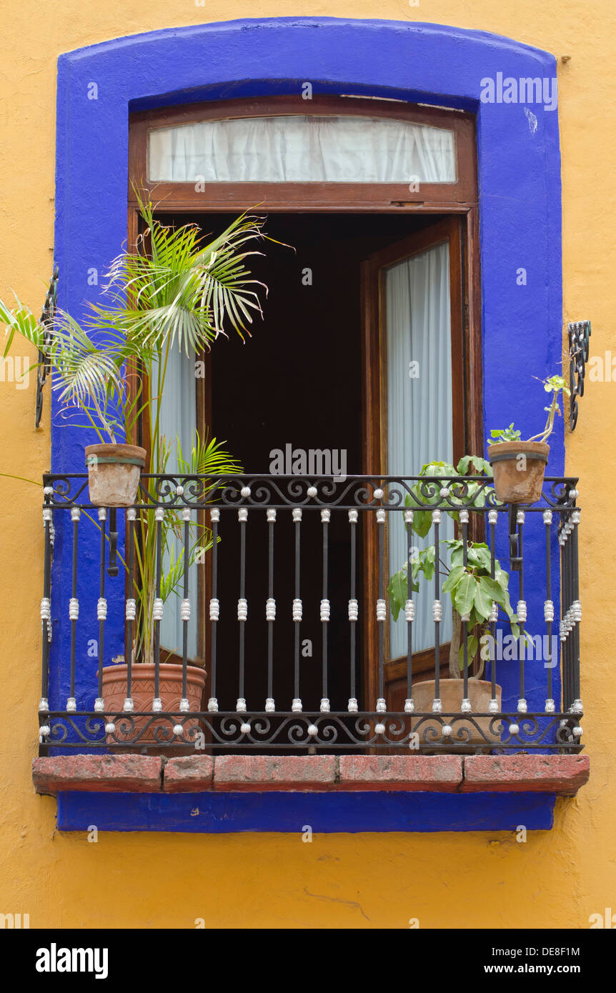 Aprire un piano superiore finestra con le piante su un piccolo balcone di un edificio in Puebla, Messico Foto Stock