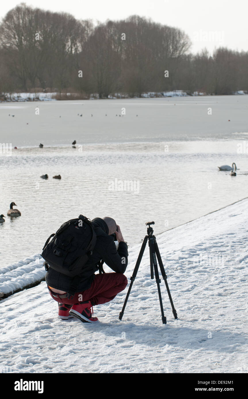 Il fotografo si accovaccia nella neve al telaio una fotografia. Foto Stock