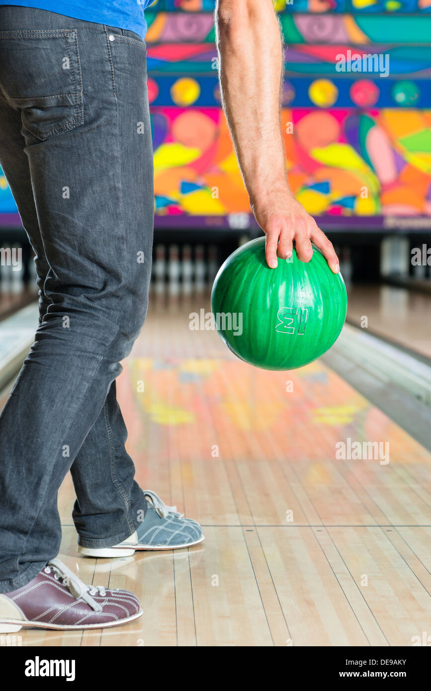 Giovane uomo in una pista da bowling avente il divertimento, l'uomo sportivo tenendo una palla da bowling di fronte alla ten pin alley Foto Stock