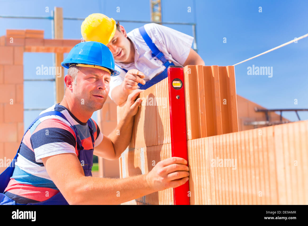 Sito in costruzione i lavoratori o muratore con caschi controllando la costruzione di pareti con una livella a bolla Foto Stock