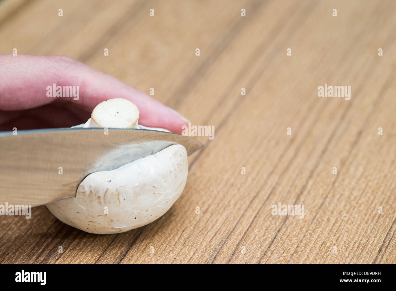 Persona per affettare un fresco Agaricus bisporus o pulsante bianco fungo con un coltello su una cucina in legno con contatore copyspace Foto Stock