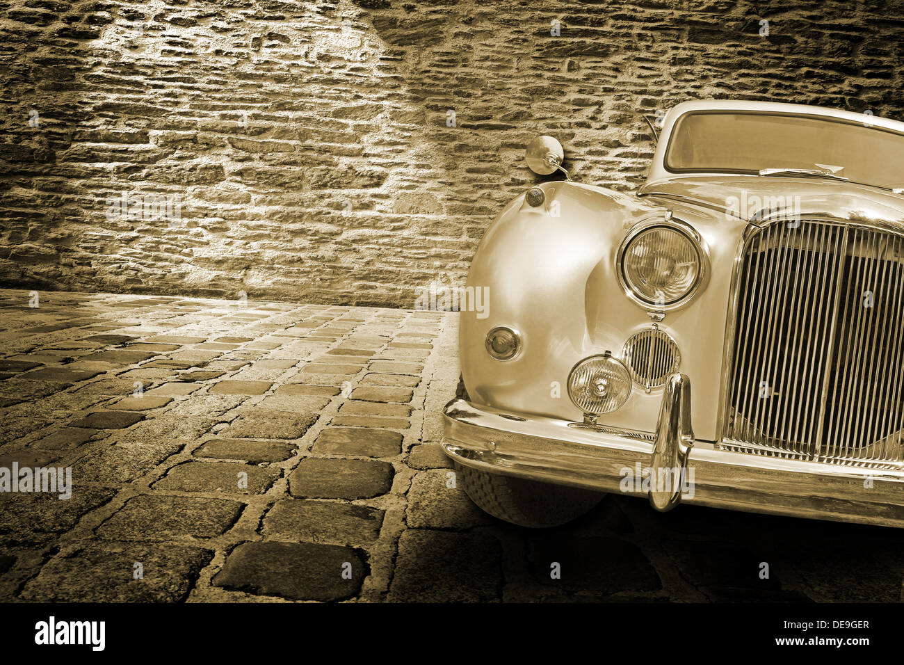 Vecchia auto sul pavimento di pietra di fronte a un muro di mattoni Foto Stock