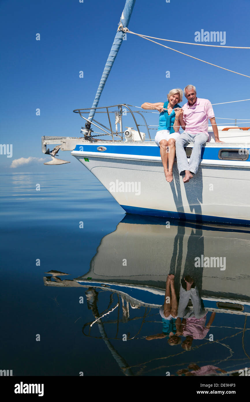 Una felice coppia senior seduto sulla parte anteriore di una imbarcazione a vela su una calma il mare blu Foto Stock