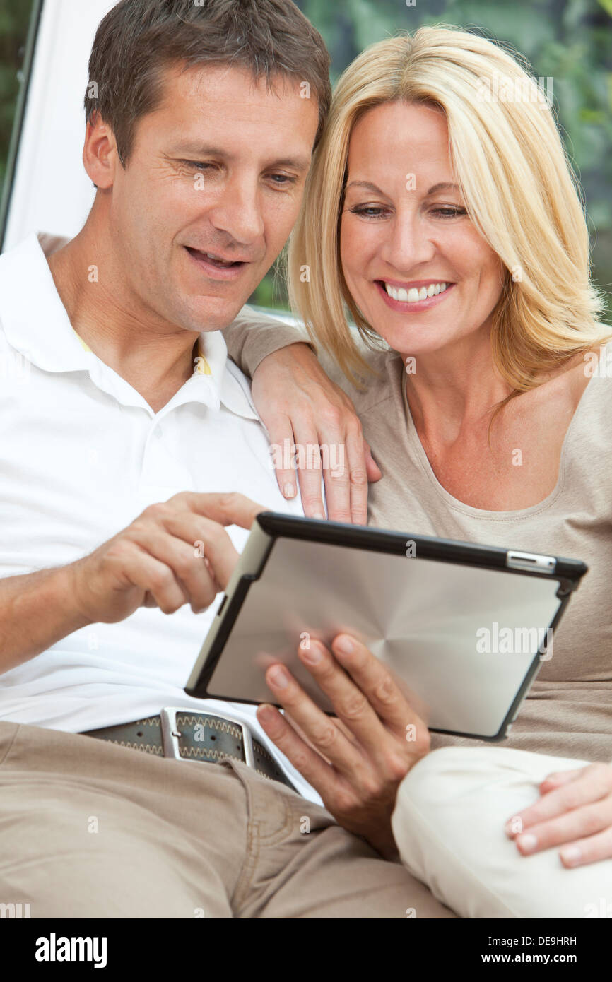 Successo e felice medio di età compresa tra un uomo e una donna matura in loro degli anni quaranta, seduti insieme a casa su un divano utilizzando computer tablet Foto Stock