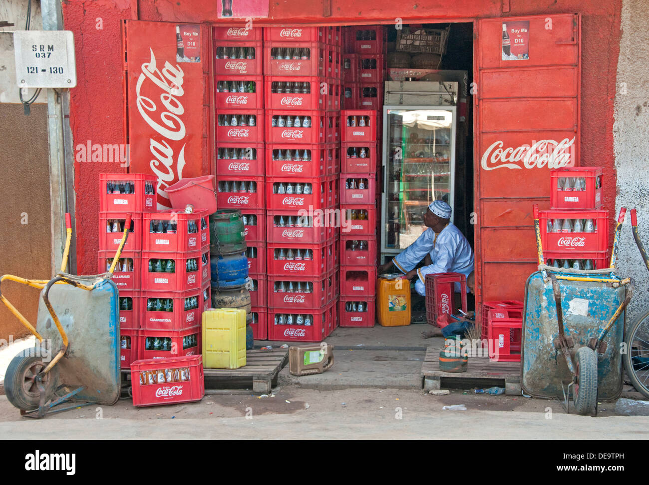 Gambiani locale l uomo nel suo negozio di vendita di Coca Cola, Serrekunda Mercato, Gambia, Africa occidentale Foto Stock