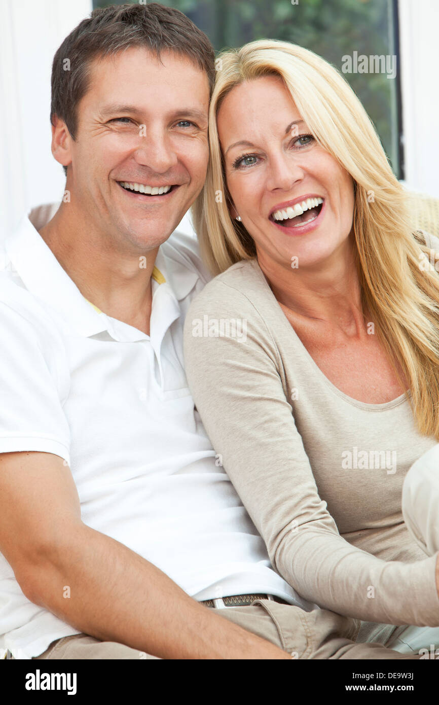 Interessante il successo di una felice uomo di mezza età & donna giovane nella loro degli anni quaranta, seduti insieme a casa sul divano, sorridente ridere Foto Stock
