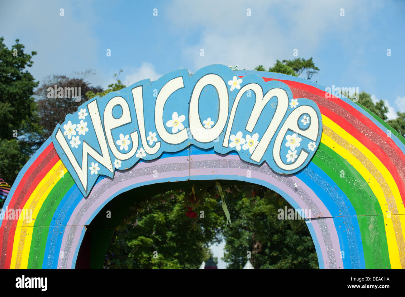 L'allegra parola benvenuti su un arcobaleno segno sopra un arco in legno al Camp Bestival festival di musica di ingresso in una giornata di sole Foto Stock