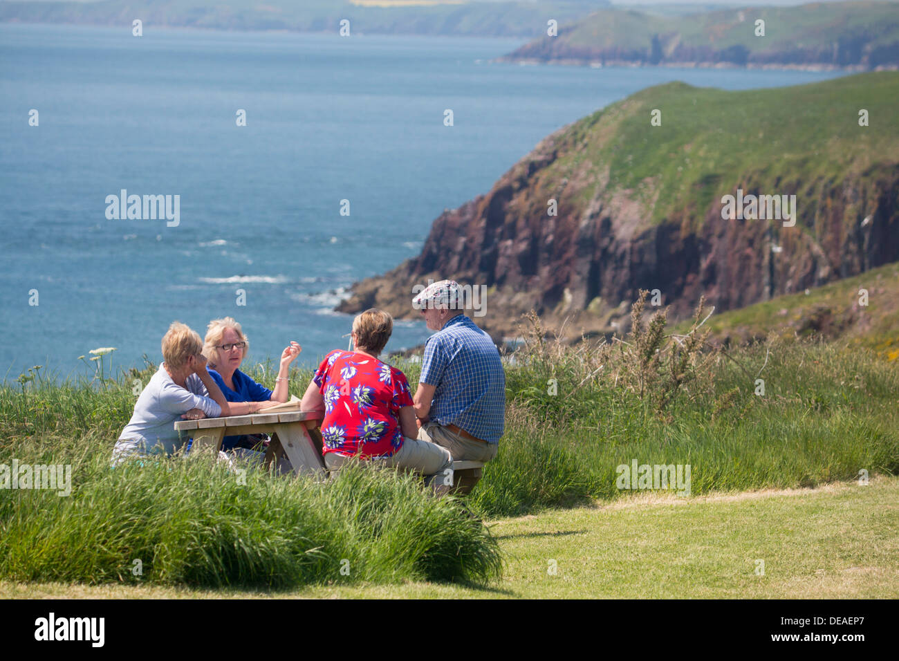 Isola di Caldey gruppo di quattro amici di mezza età 50s seduti attorno al tavolo di gioco in chat costa e mare dietro il Pembrokeshire Wales UK Foto Stock