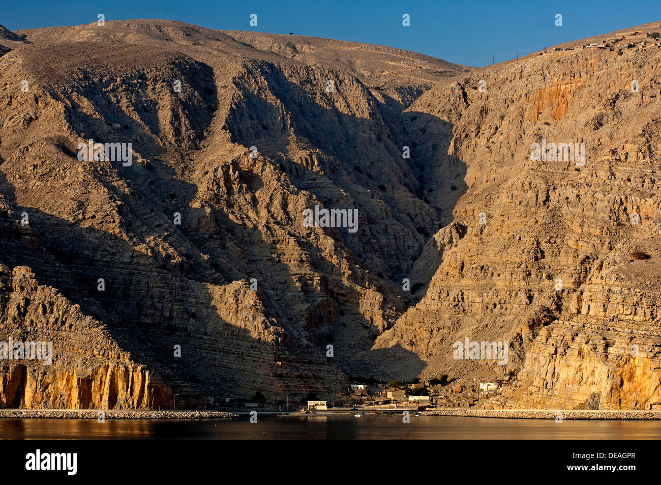 Piccolo villaggio nella luce del mattino ai piedi delle scogliere rocciose di un fiordo nella penisola di Musandam sul Golfo Persico Foto Stock