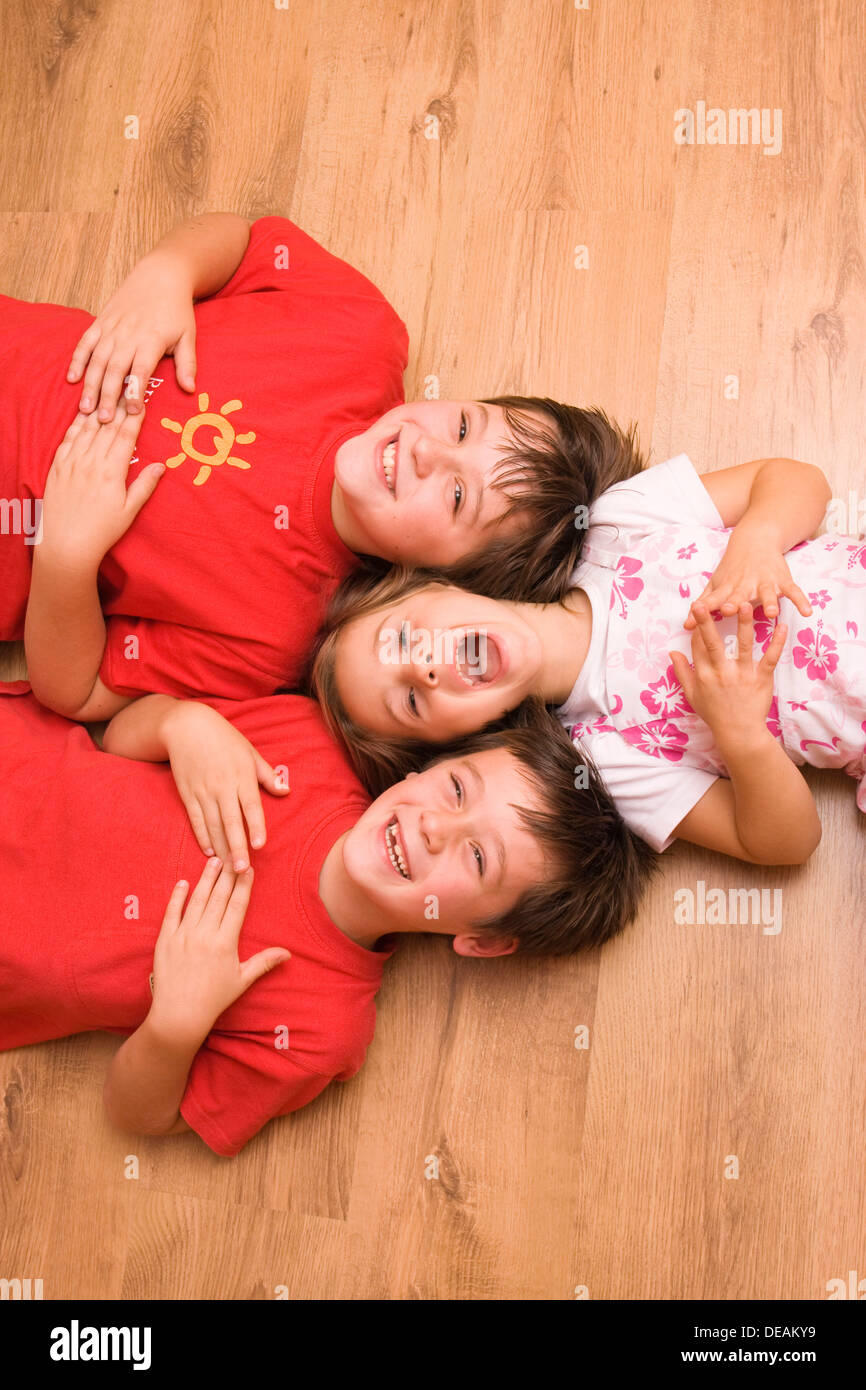 Ragazza 4 anni, e i ragazzi di 6 e 11 anni, sdraiato sul pavimento, ridendo Foto Stock