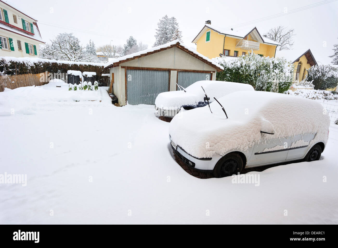 Scena di neve. Due automobili parcheggiate essendo coperte da neve. Essi non sono in garage (in background) Foto Stock