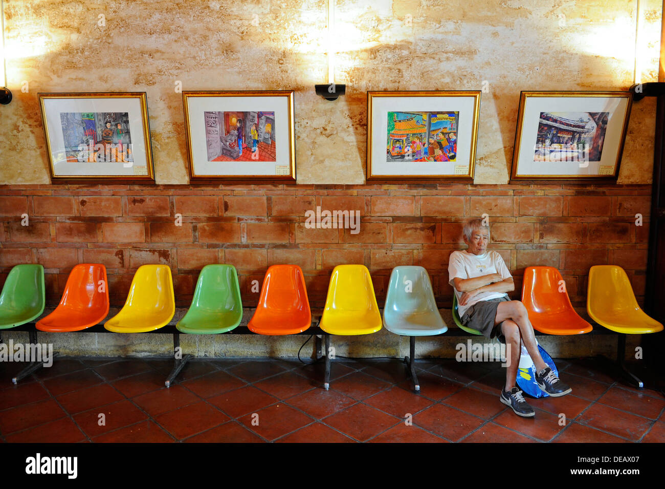 Il vecchio uomo che indossa pantaloni corti e t-shirt seduto su una fila di  plastica colorata sedie con dipinti colorati Foto stock - Alamy
