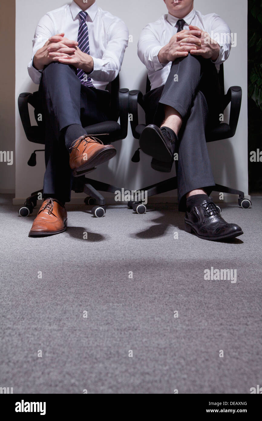 Due imprenditori seduti con le gambe incrociate, sezione bassa Foto Stock