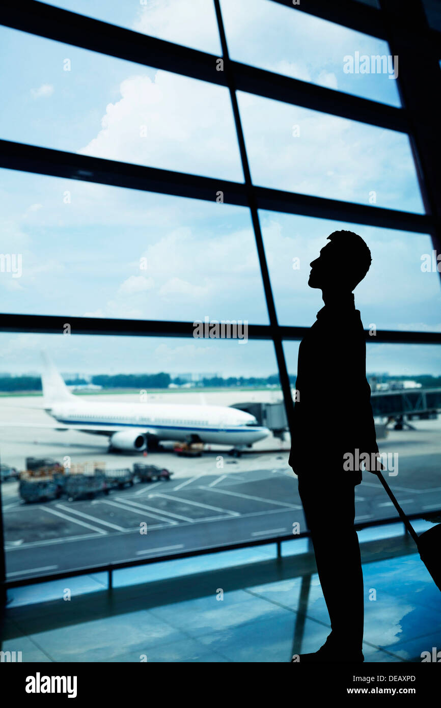 Silhouette di imprenditore in attesa in aeroporto e guardando fuori dalla finestra Foto Stock
