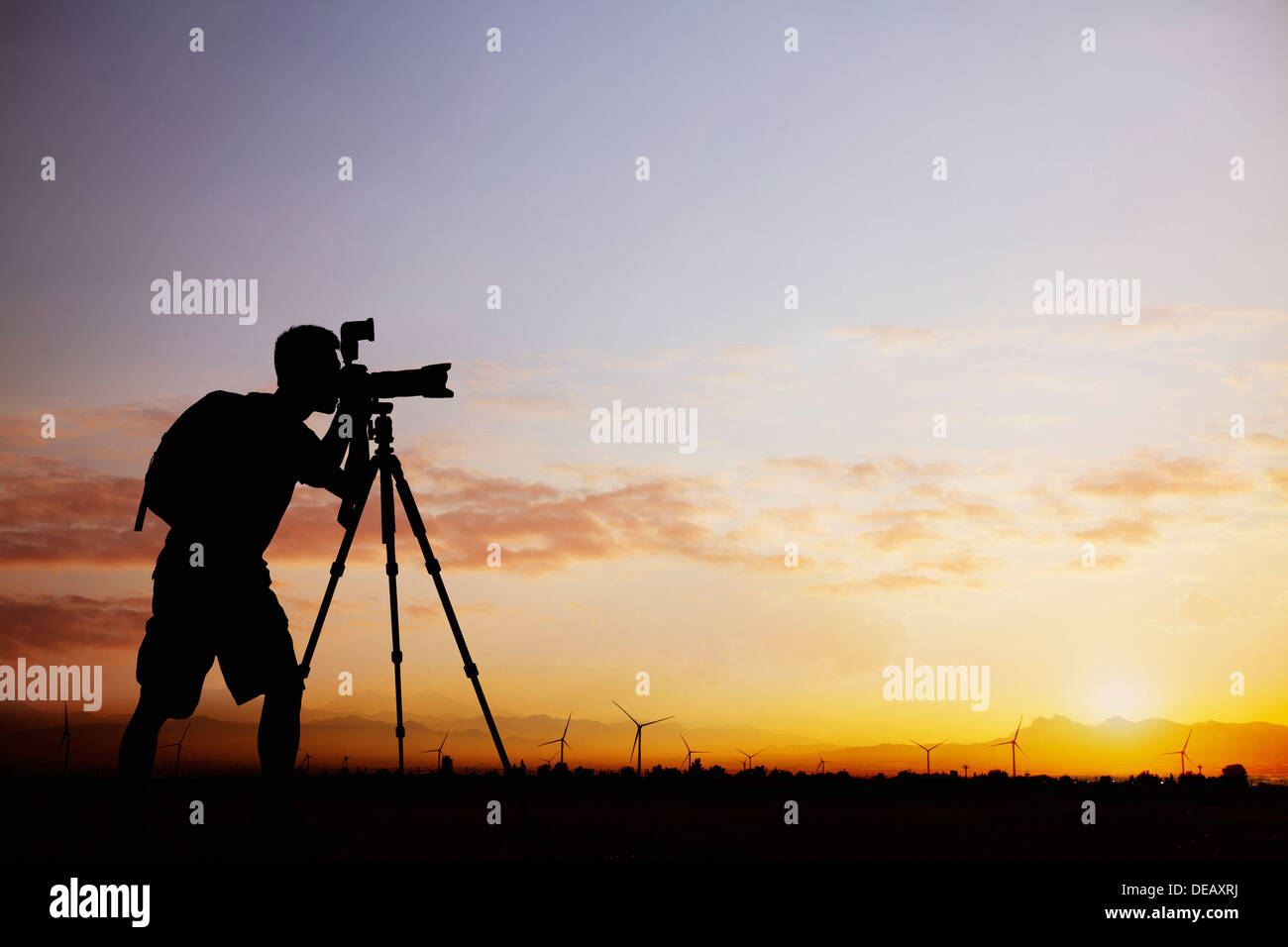 Silhouette di uomo di scattare le foto con la sua macchina fotografica al tramonto con un cielo drammatico Foto Stock