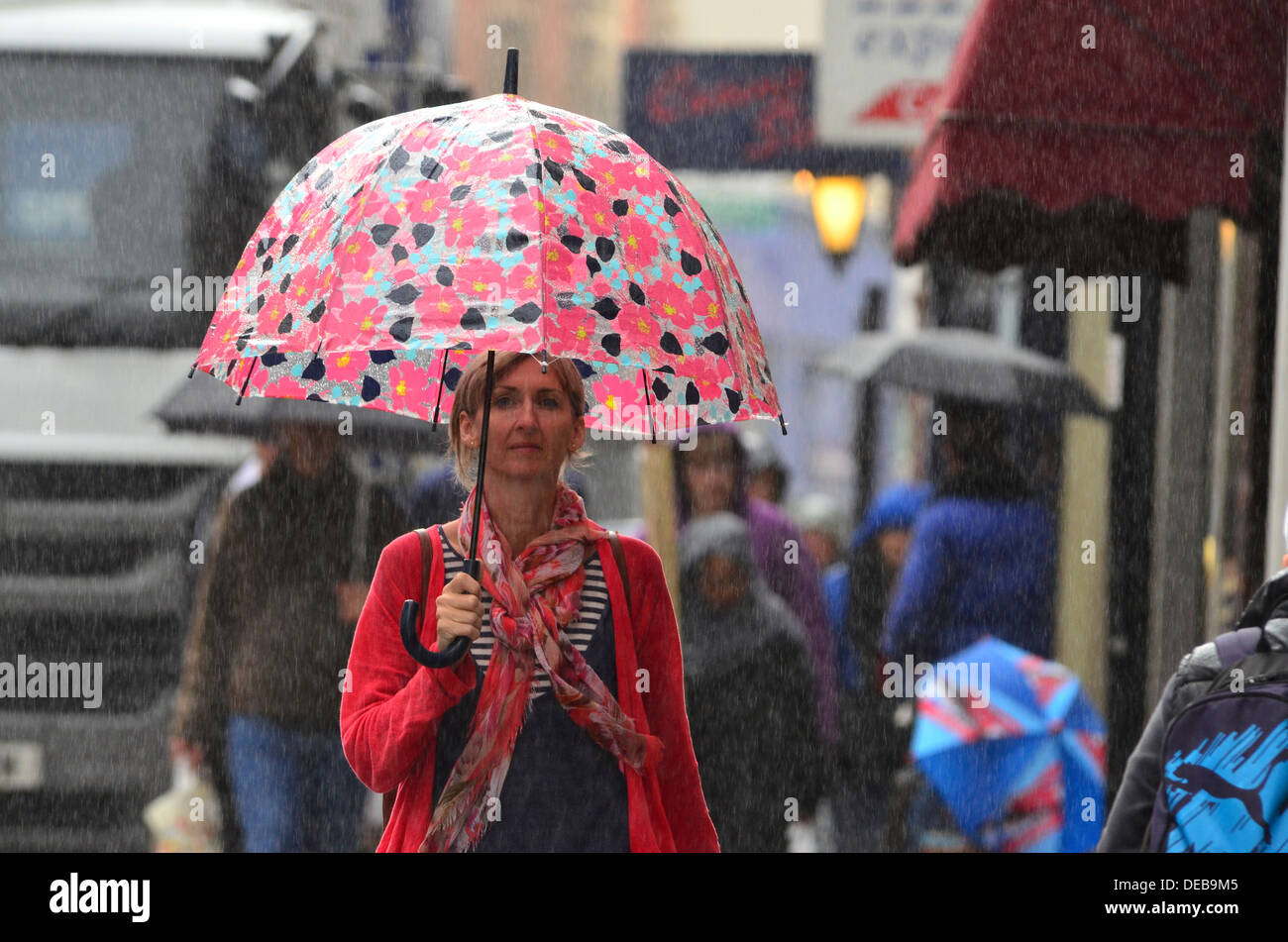 Donna che cammina con ombrello in caso di pioggia in una trafficata strada alta Foto Stock